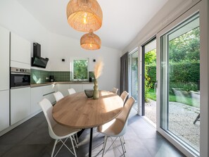 Una cocina moderna con una mesa redonda para comer, sillas blancas y un ventanal con vistas al jardín.
