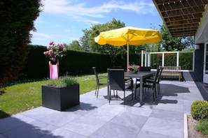 Un patio al aire libre con una mesa, sillas, un paraguas amarillo y plantas en macetas.