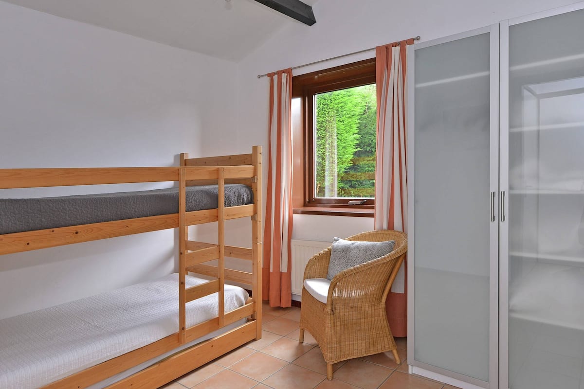 Una habitación con una cama individual, una silla de mimbre y un armario.