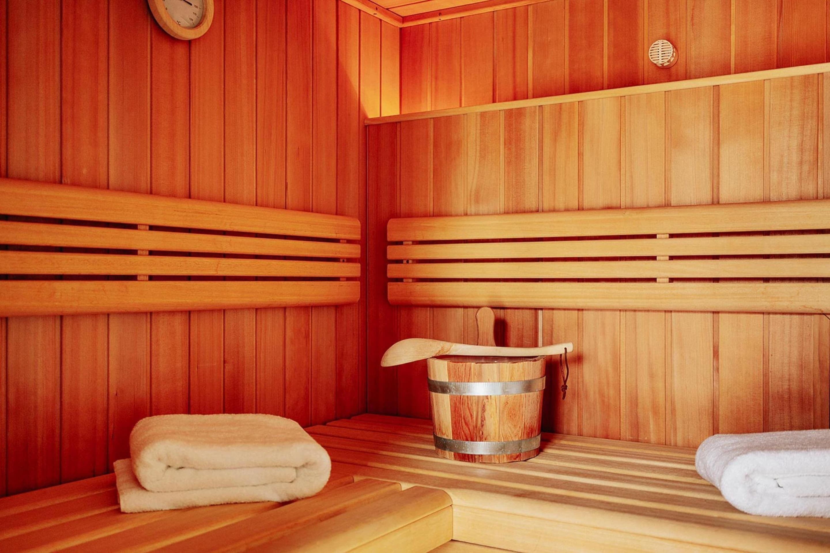 A sauna room with wooden benches, a wooden bucket, and towels.