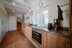 A kitchen with wooden cabinets, a stainless steel oven, a coffee maker, and a window with a view. - Holiday Homes in Torfhaus Harzresort, Torfhaus (Clausthal-Zellerfeld)