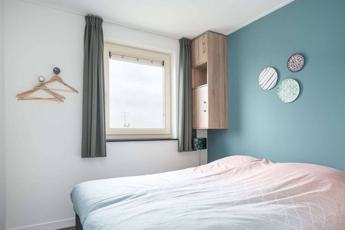 A bedroom with a bed, a window with curtains, a wooden wardrobe, and decorative plates on the wall.