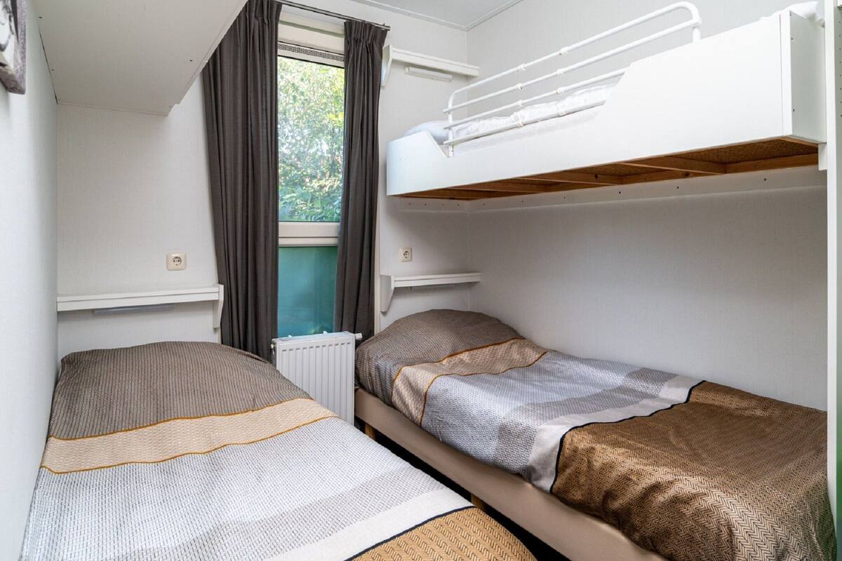 A compact room with two bunk beds, a window with curtains, and a radiator.