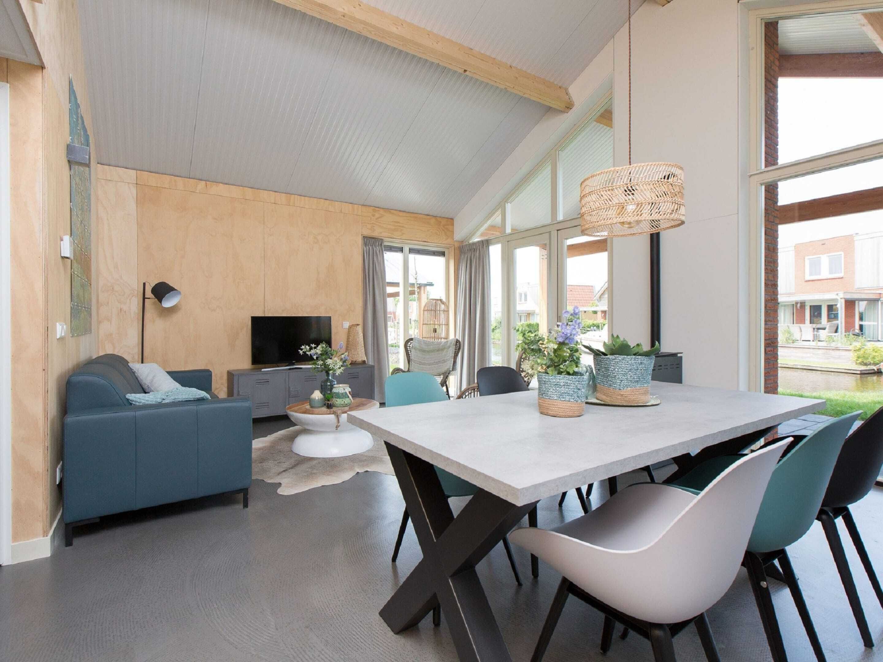 A modern living room with a sofa, TV, and dining area with chairs and a table.