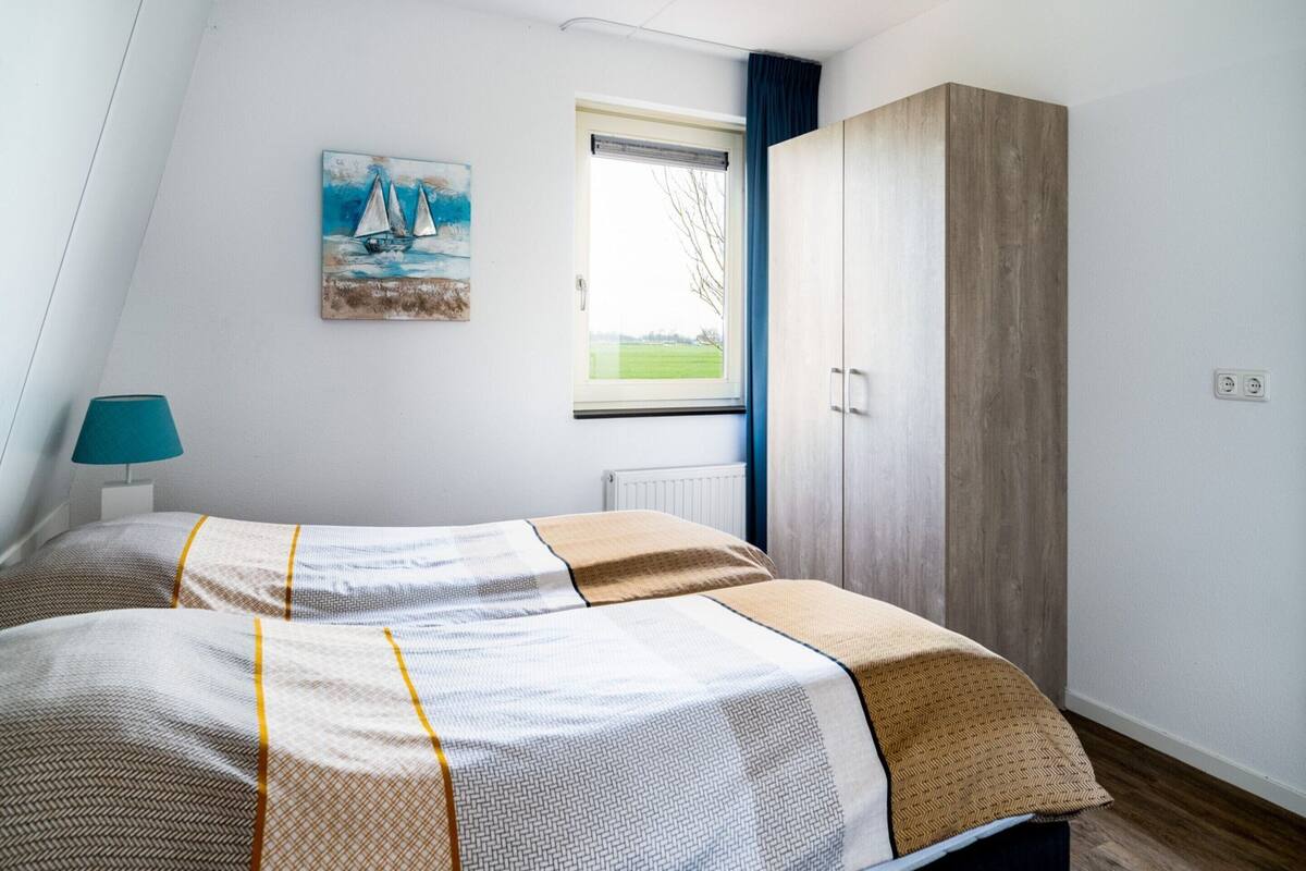 A bedroom with a bed, a window with a view, a painting, and a wardrobe.
