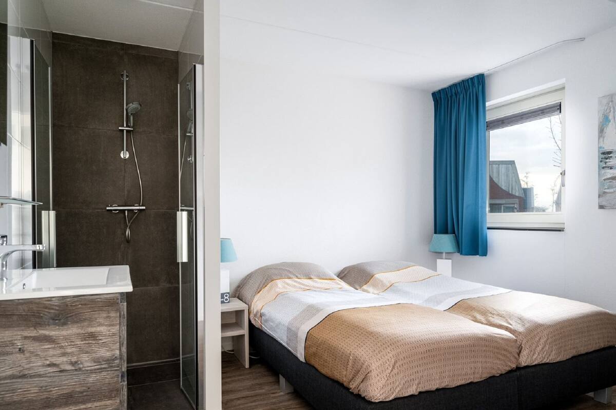 A modern hotel room with a shower, a bed, a bedside table, and a window with curtains.