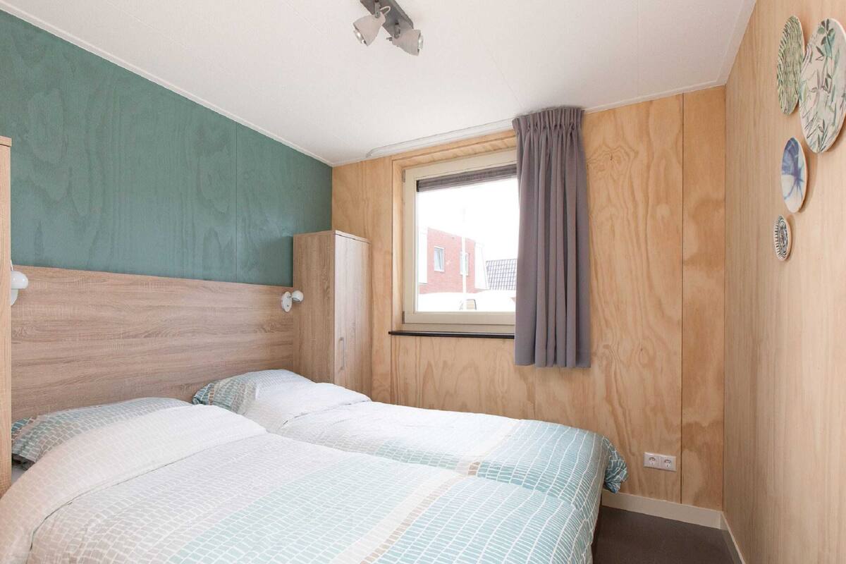 A bedroom with two beds, wooden headboard, a window with curtains, and a wall-mounted cabinet.