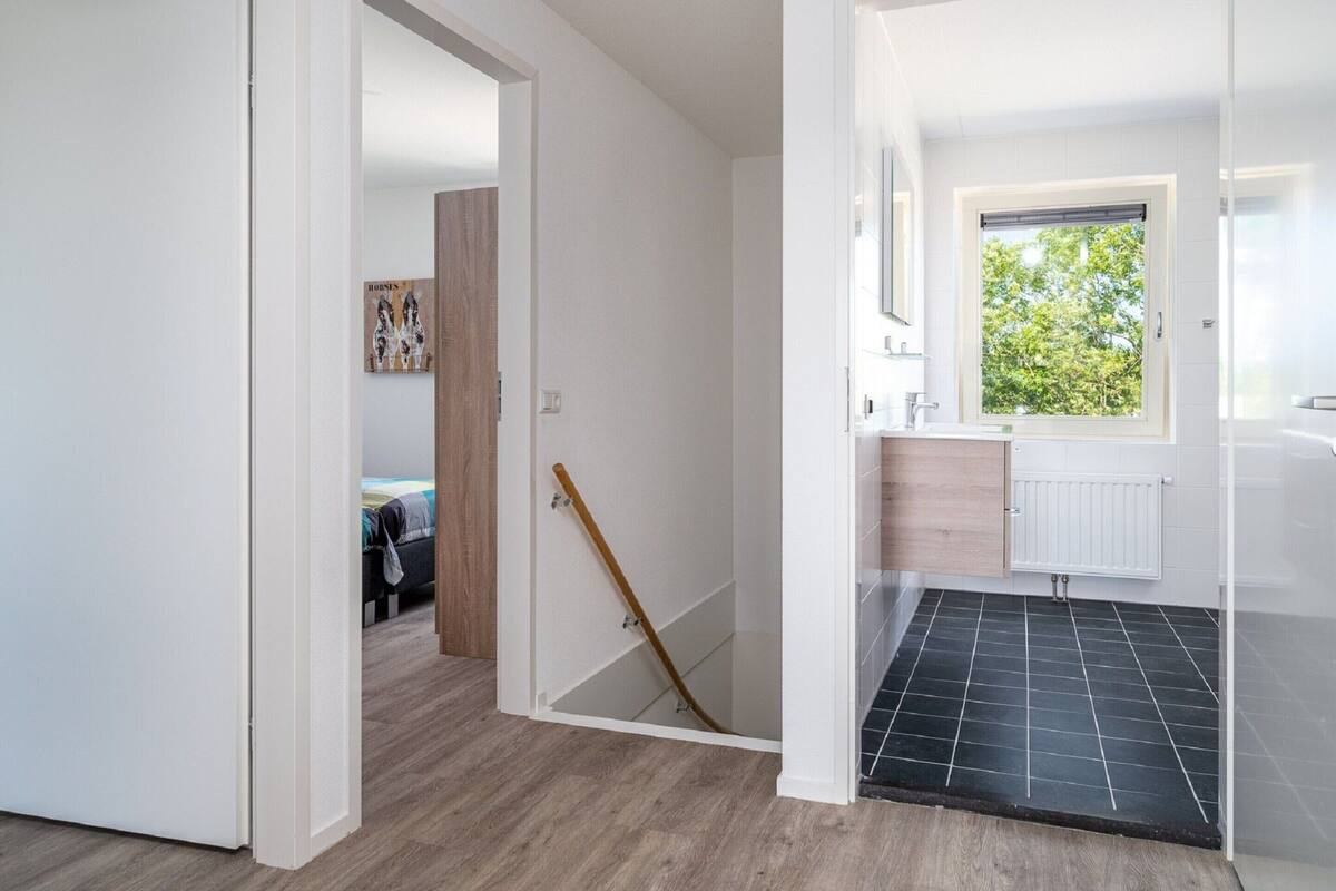 A modern bathroom with a window, a shower area, and a visible door leading to another room.