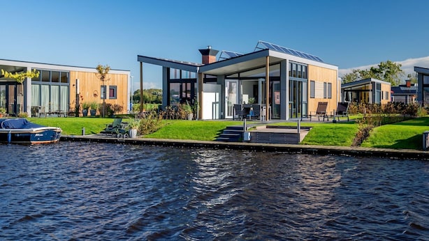A modern waterfront property with a glass-roofed central building, a covered outdoor seating area, and a canal in the foreground. - Bungalow With an Outdoor Fireplace by Water (Akkrum)