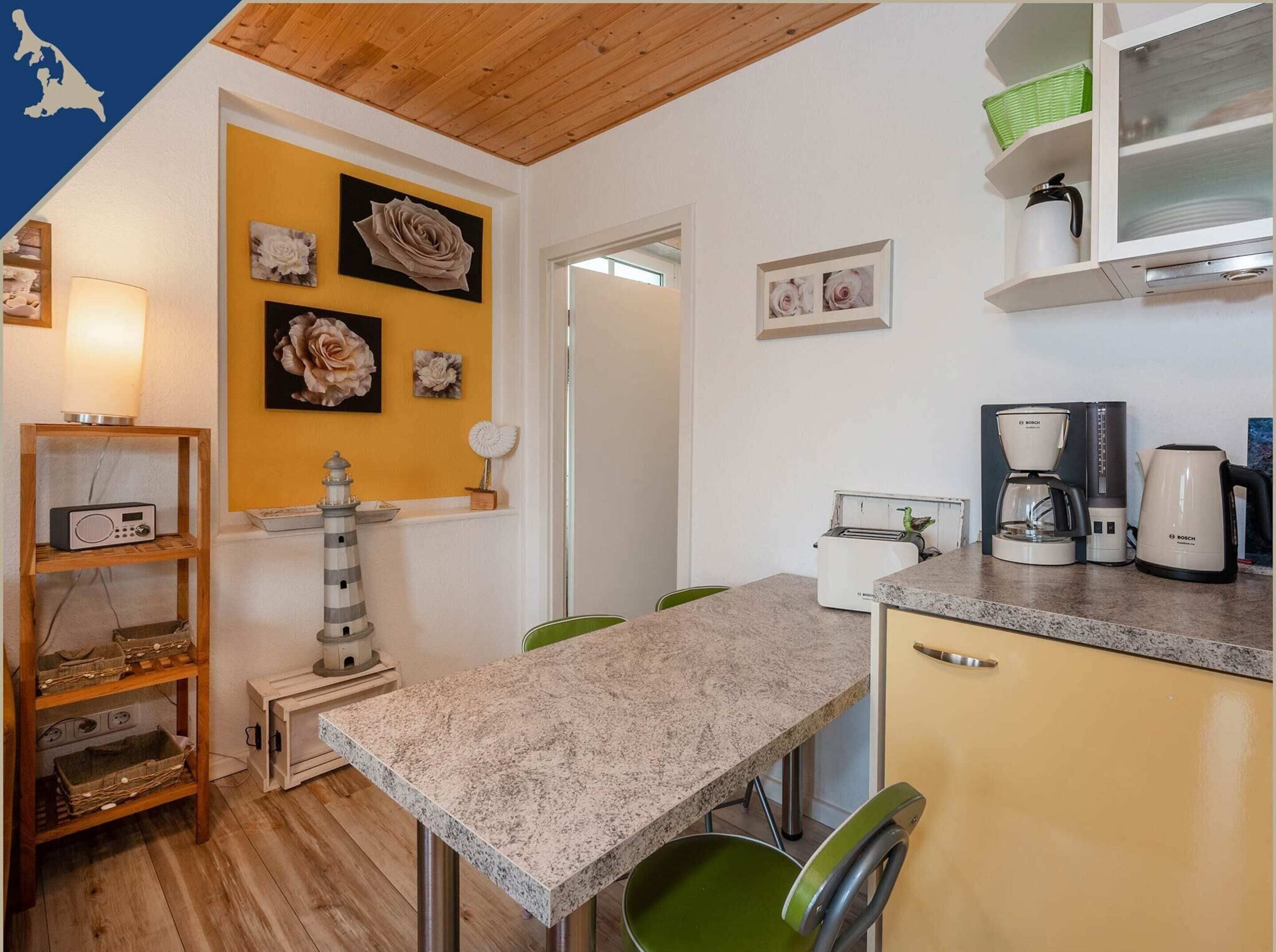 A compact kitchen with a granite countertop, a Bosch coffee maker, and a toaster. There are decorative wall art pieces and a lighthouse model on a shelf.