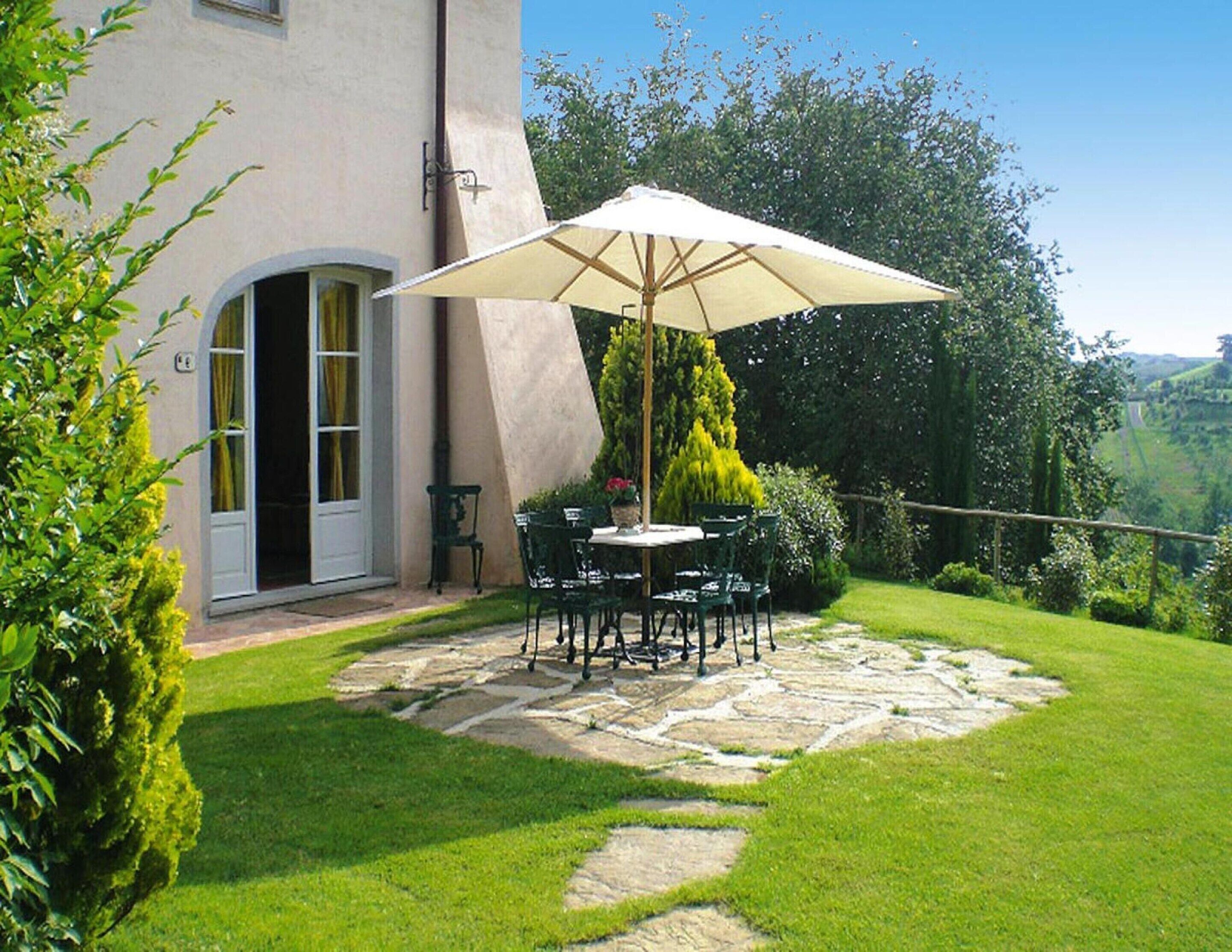 A patio with a stone pathway, a table, chairs, and an umbrella.