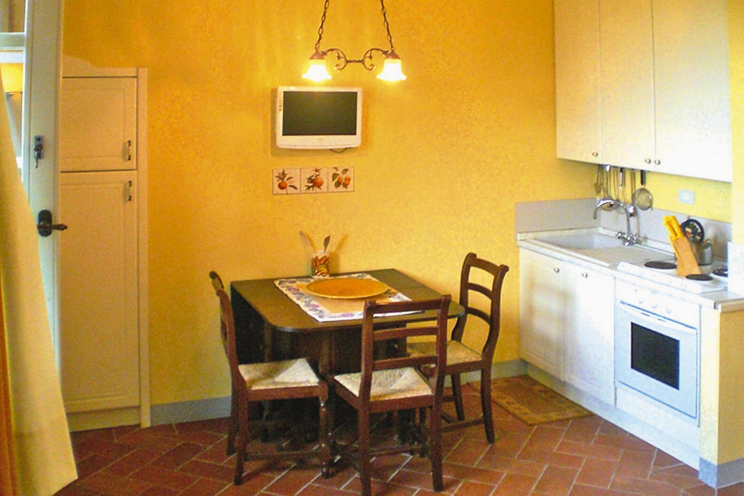 Een kleine keuken met een eettafel, stoelen, een kleine televisie en basisapparatuur.