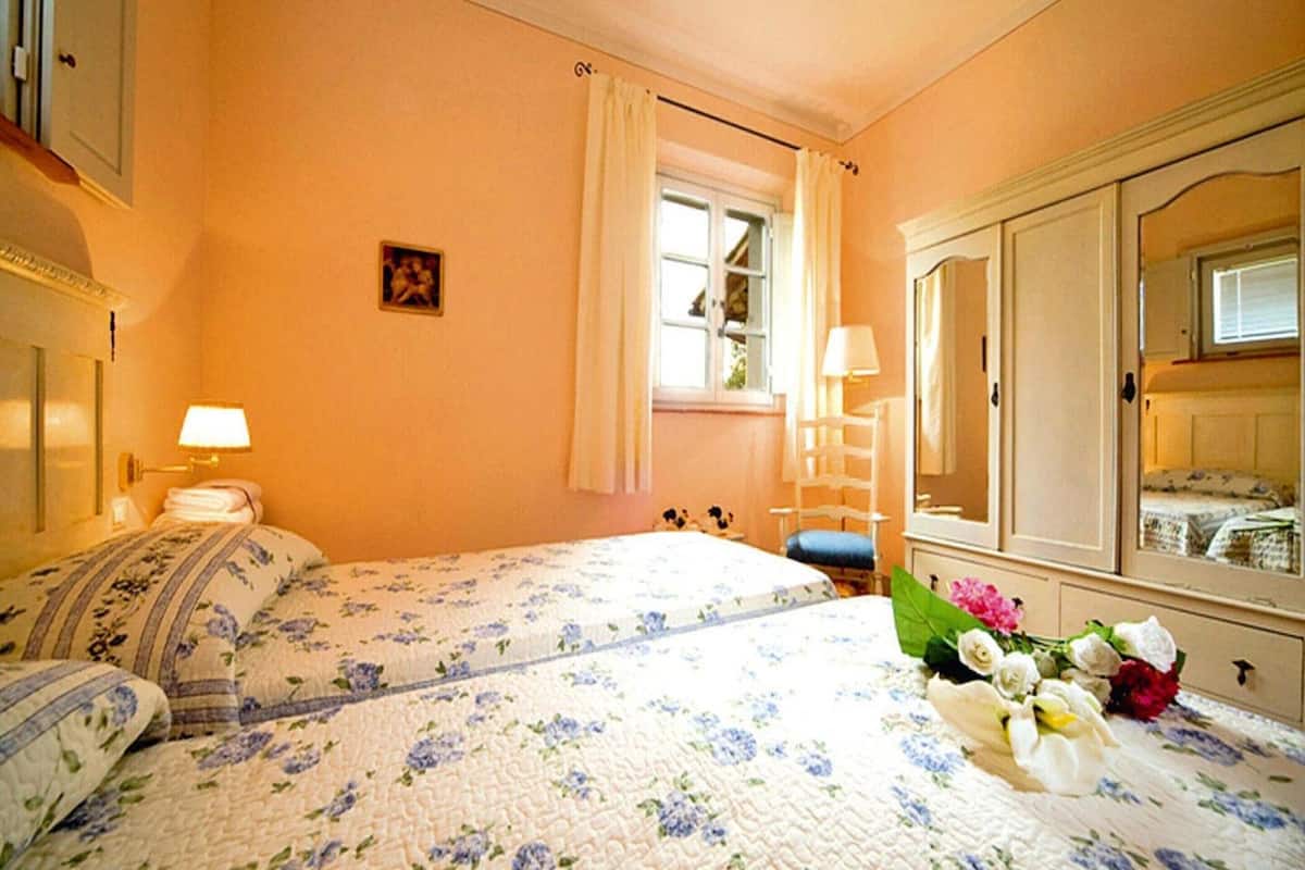 A hotel room with a bed, a nightstand, a dresser with a mirror, a window with curtains, and a small picture on the wall.