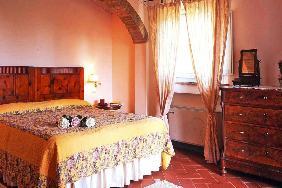 A bedroom with a wooden headboard, a bed with a floral bedspread, a dresser, and a window with curtains.