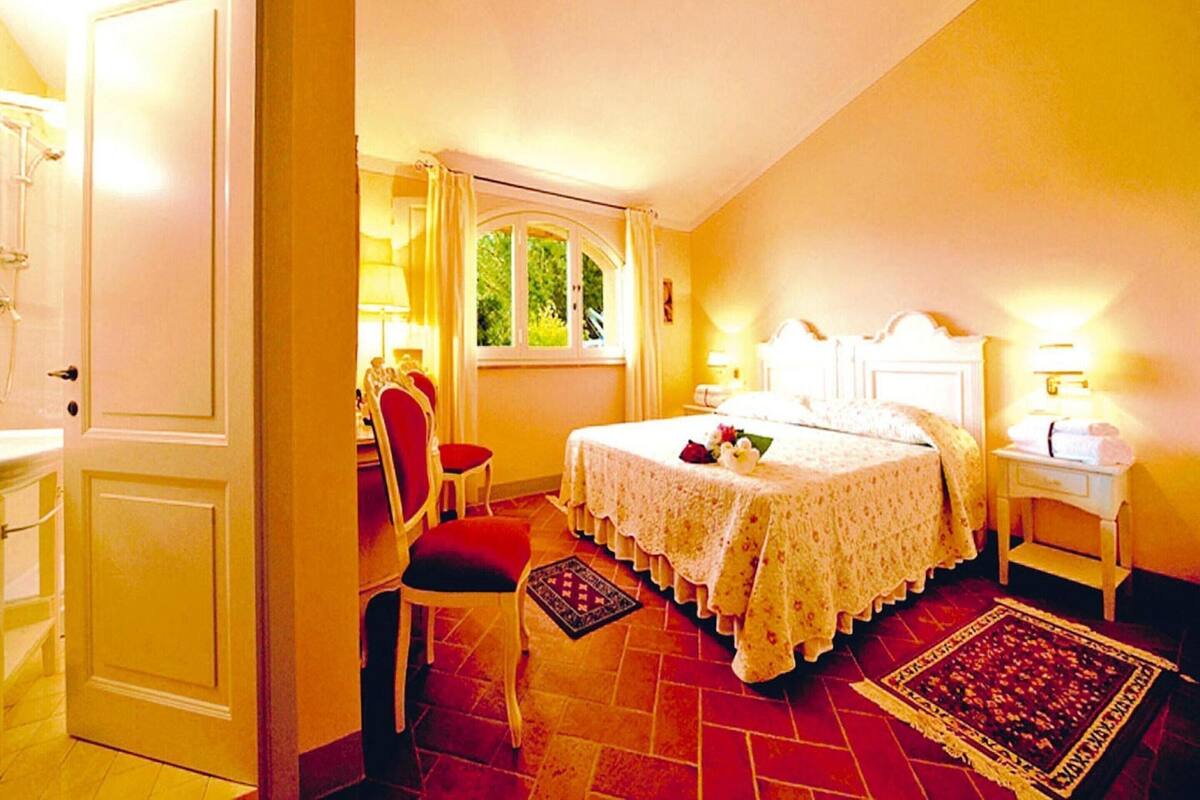 A bedroom with a bed, a chair, a nightstand, a window, and a door.