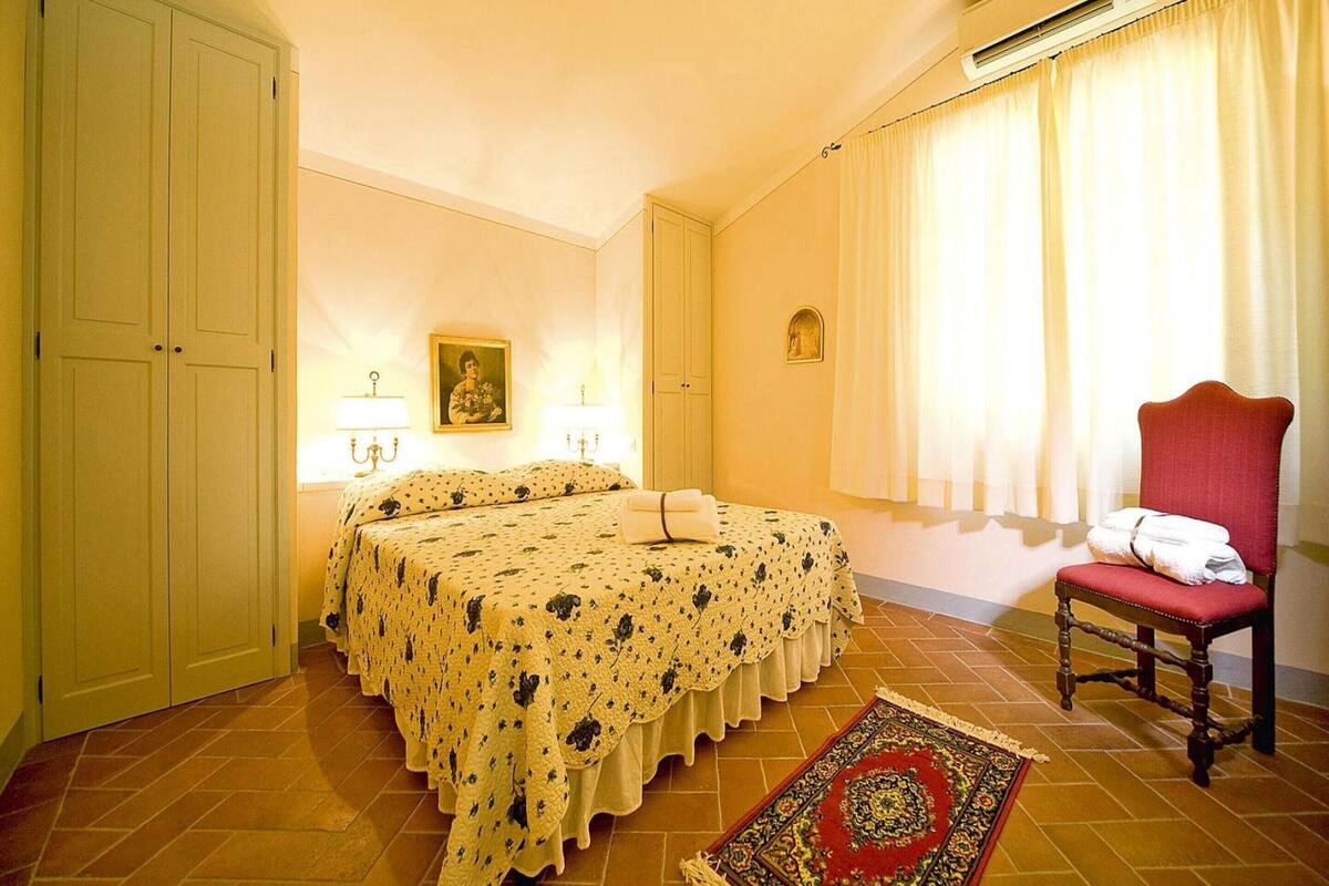 A hotel room with a double bed, a red armchair, a patterned rug, and a painting on the wall.
