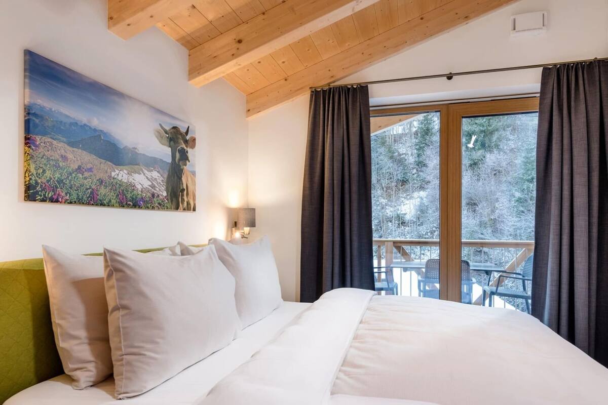 Un dormitorio con una cama, un cuadro, una mesita de noche y vistas al exterior.