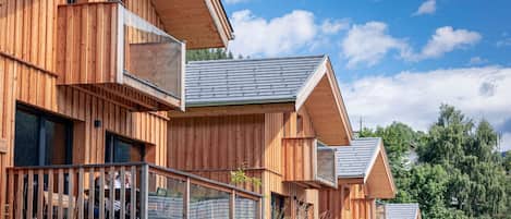A row of wooden cabins with large windows and balconies, set in a natural landscape.
