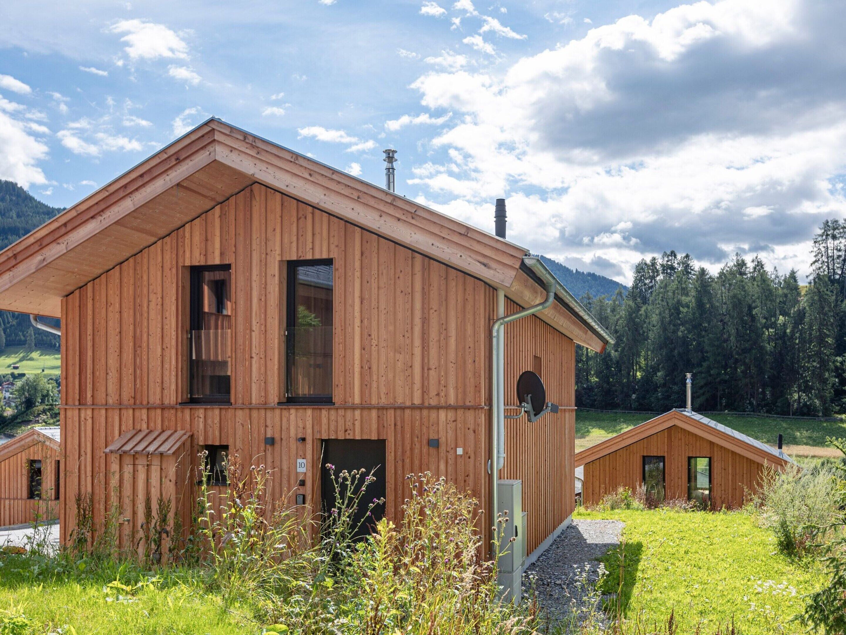 Una cabaña de madera con techo inclinado, ventanas amplias y una chimenea.