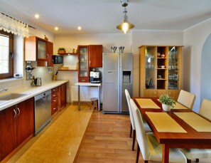 A compact kitchen with wooden cabinets, a built-in microwave, a refrigerator, and a dining area with a table and chairs. - Holiday Homes, Kolobrzeg (Kolobrzeg)