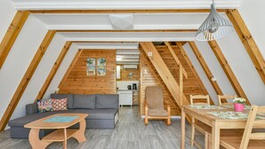 A loft-style room with a wooden ceiling, a sofa, a coffee table, a dining table with chairs, and a hanging light fixture. - Holiday Homes, Kolobrzeg (Kolobrzeg)