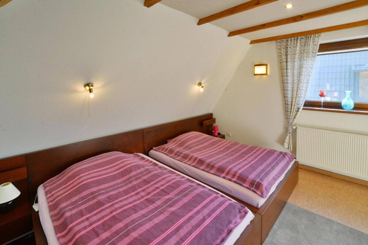 A bedroom with two beds, wooden beams on the ceiling, and a window with curtains.
