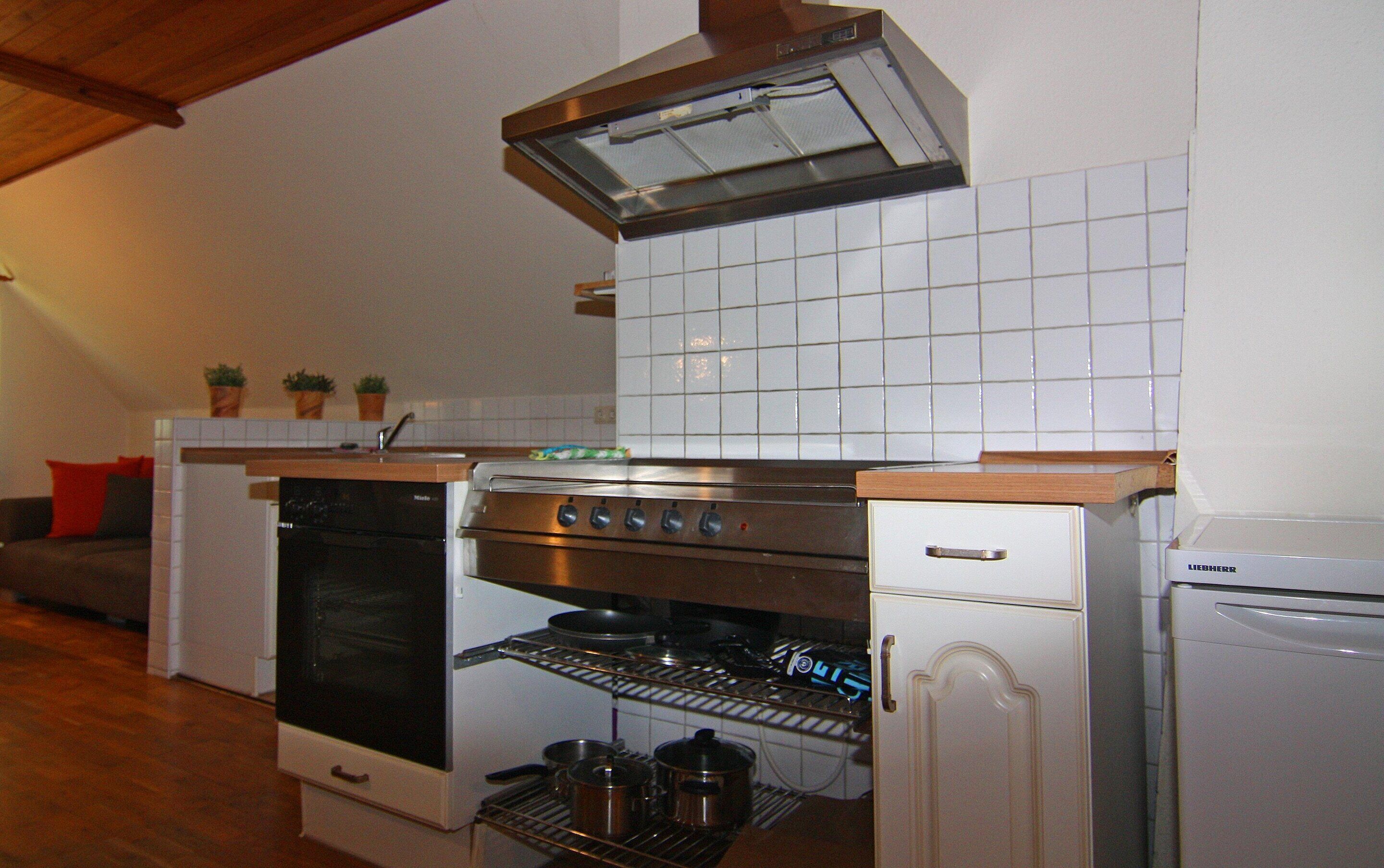 Eine kompakte Küche mit Einbauofen, Mikrowelle und Geschirrspüler. Die Decke besteht aus Holz und die Rückwand ist mit Fliesen verkleidet.