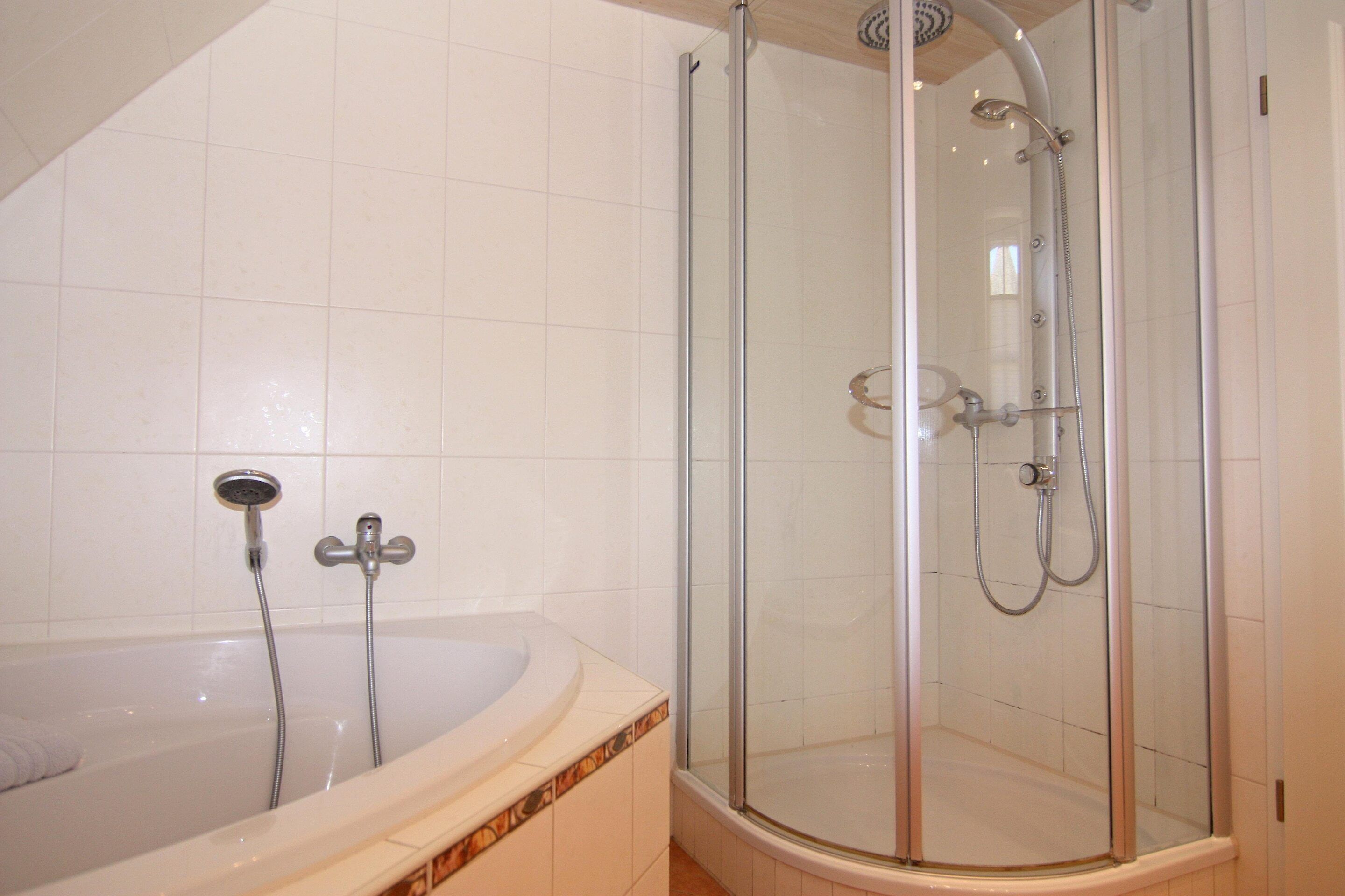 Ein Badezimmer mit einer gläsernen Duschkabine, einer Badewanne und einer separaten Duschbrause.