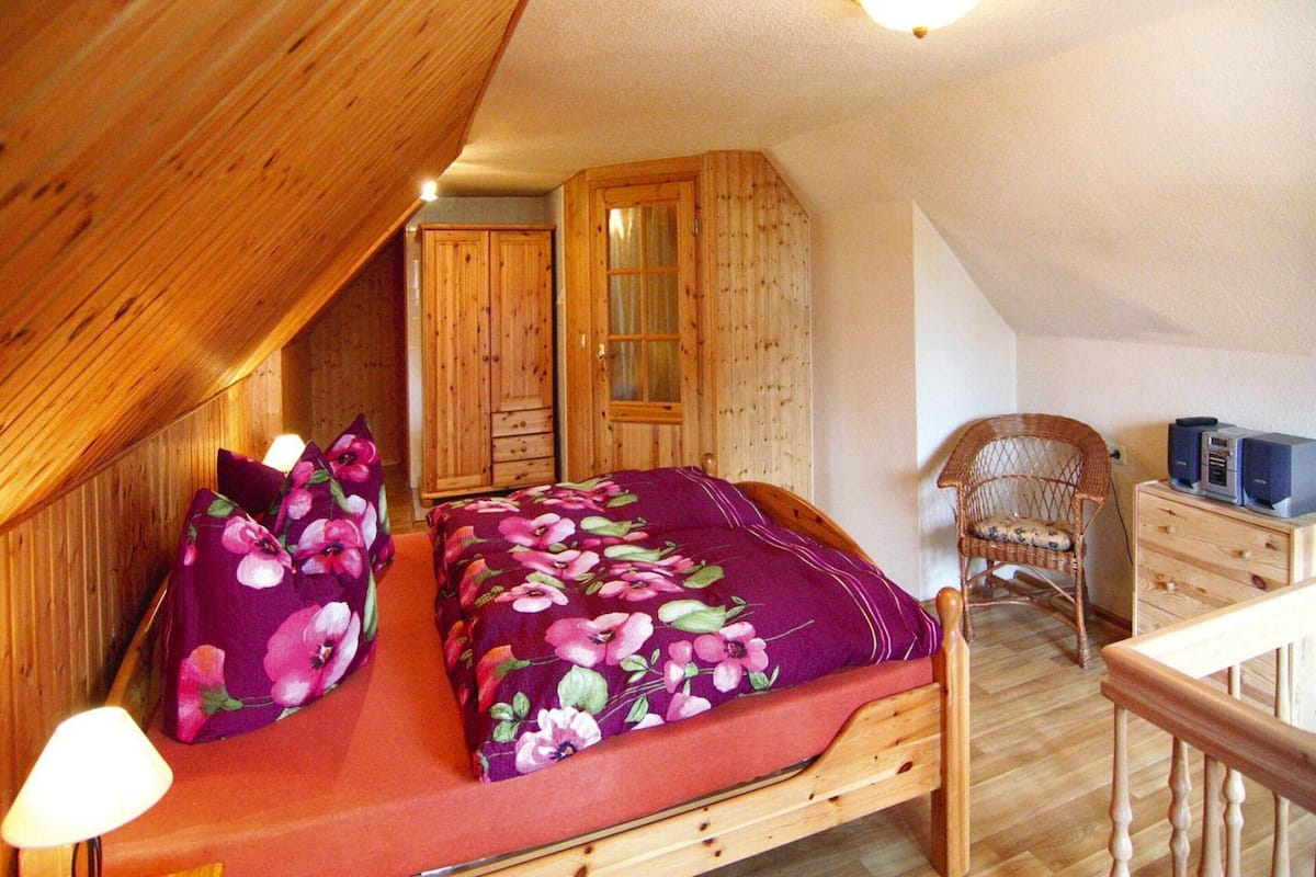 A bedroom with a wooden bed, a nightstand, a lamp, a wardrobe, and a chair.