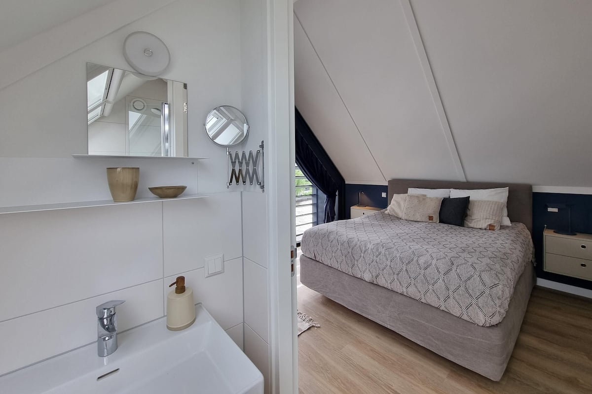 A bedroom with a bed, a bedside table, a nightstand, a mirror, a shelf with a bowl, and a towel rack.