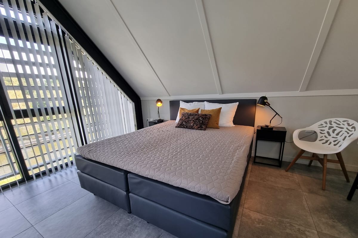 A bedroom with a bed, bedside tables, a chair, and a view through a window with blinds.