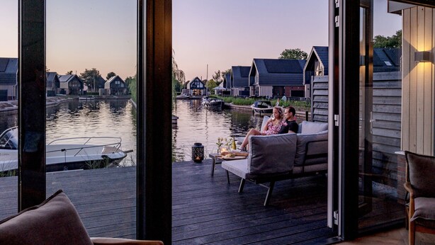 Ett modernt utomhusområde med sittplatser och utsikt över en kanal och traditionella hus.