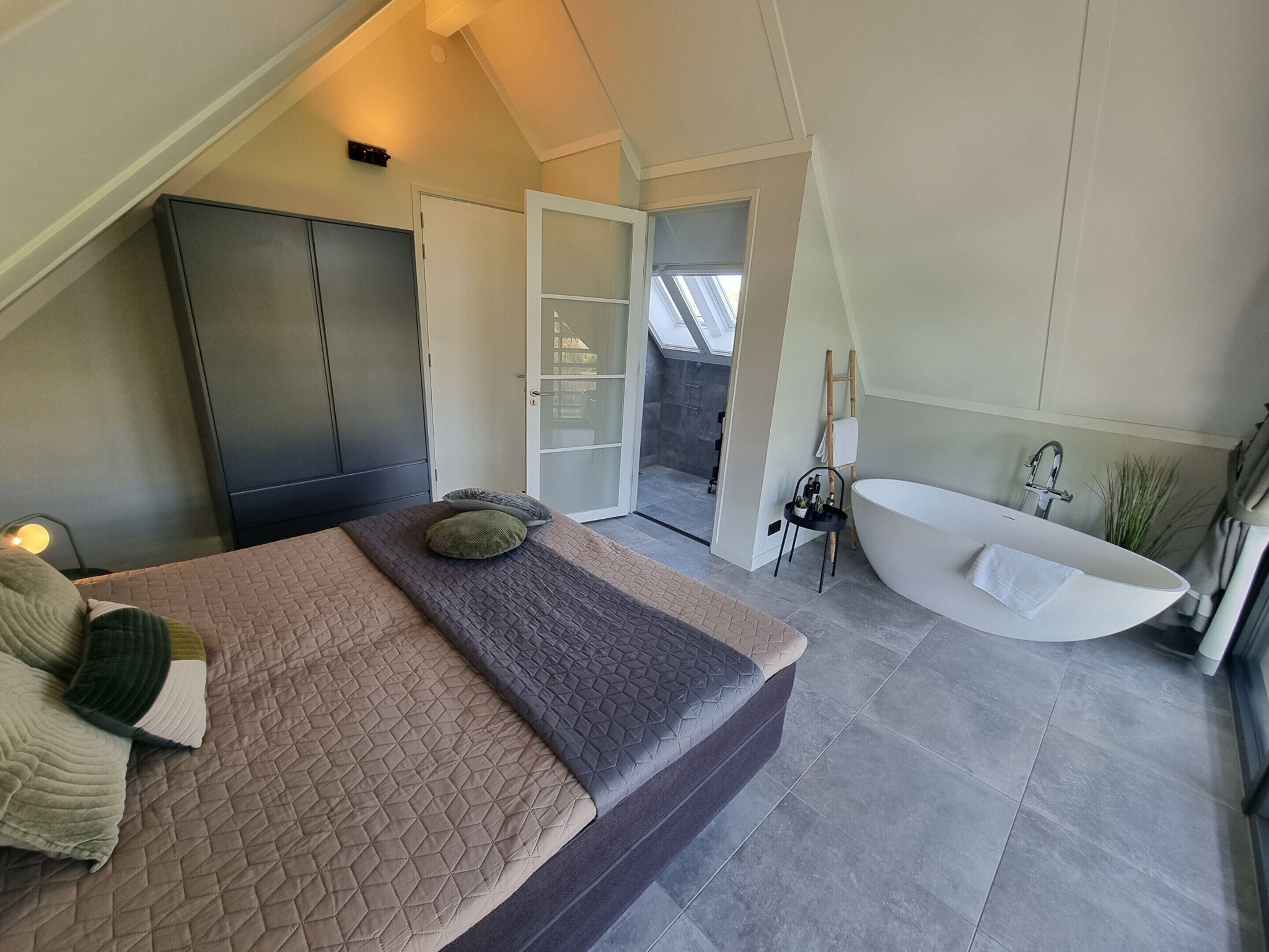 Una camera da letto con un letto, un armadio, un bagno con vasca e un lucernario.
