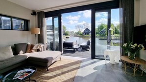 Ett modernt vardagsrum med en soffa, ett soffbord och utsikt över en vattenyta och byggnader.
