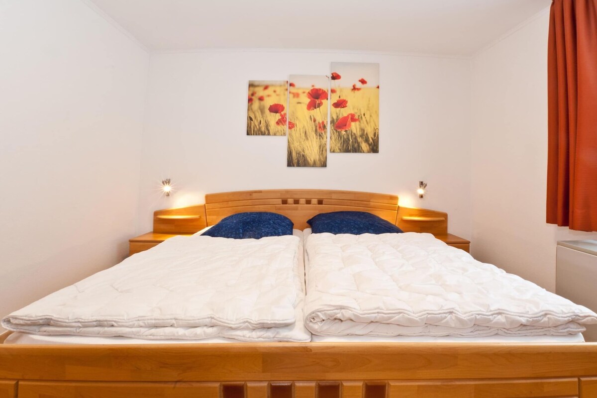 A double bed with a wooden headboard, two bedside tables with lamps, and three wall-mounted paintings of red flowers.
