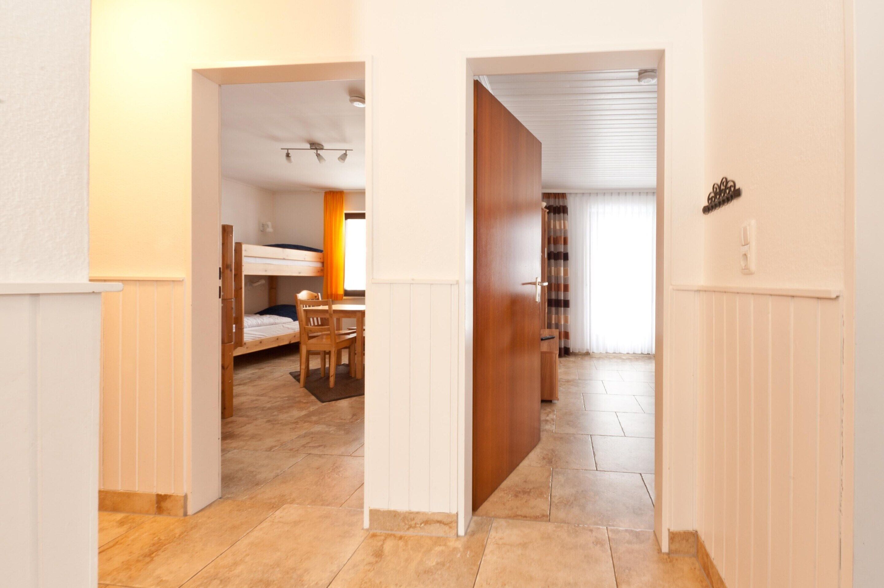 Una habitación con una cama nido, una mesa de comedor con sillas y una puerta corredera que da a otra habitación.