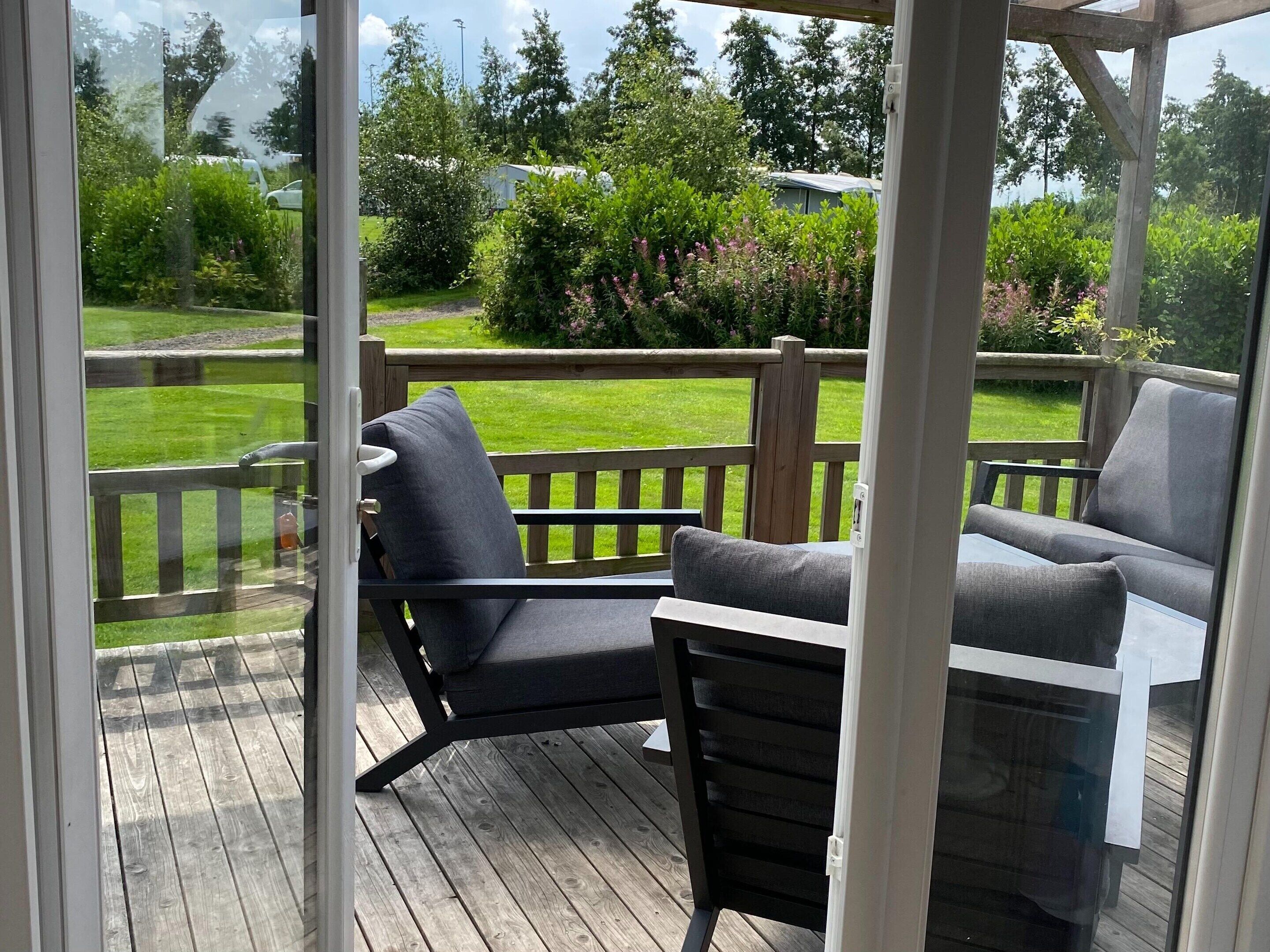 En overdækket terrasse med to grå polstrede stole og et lille bord.