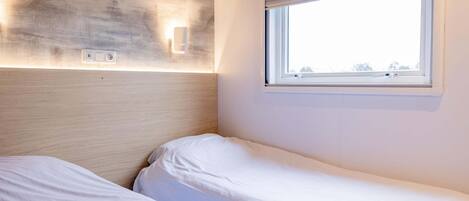 A room with two beds, a window with blinds, and a textured wall.