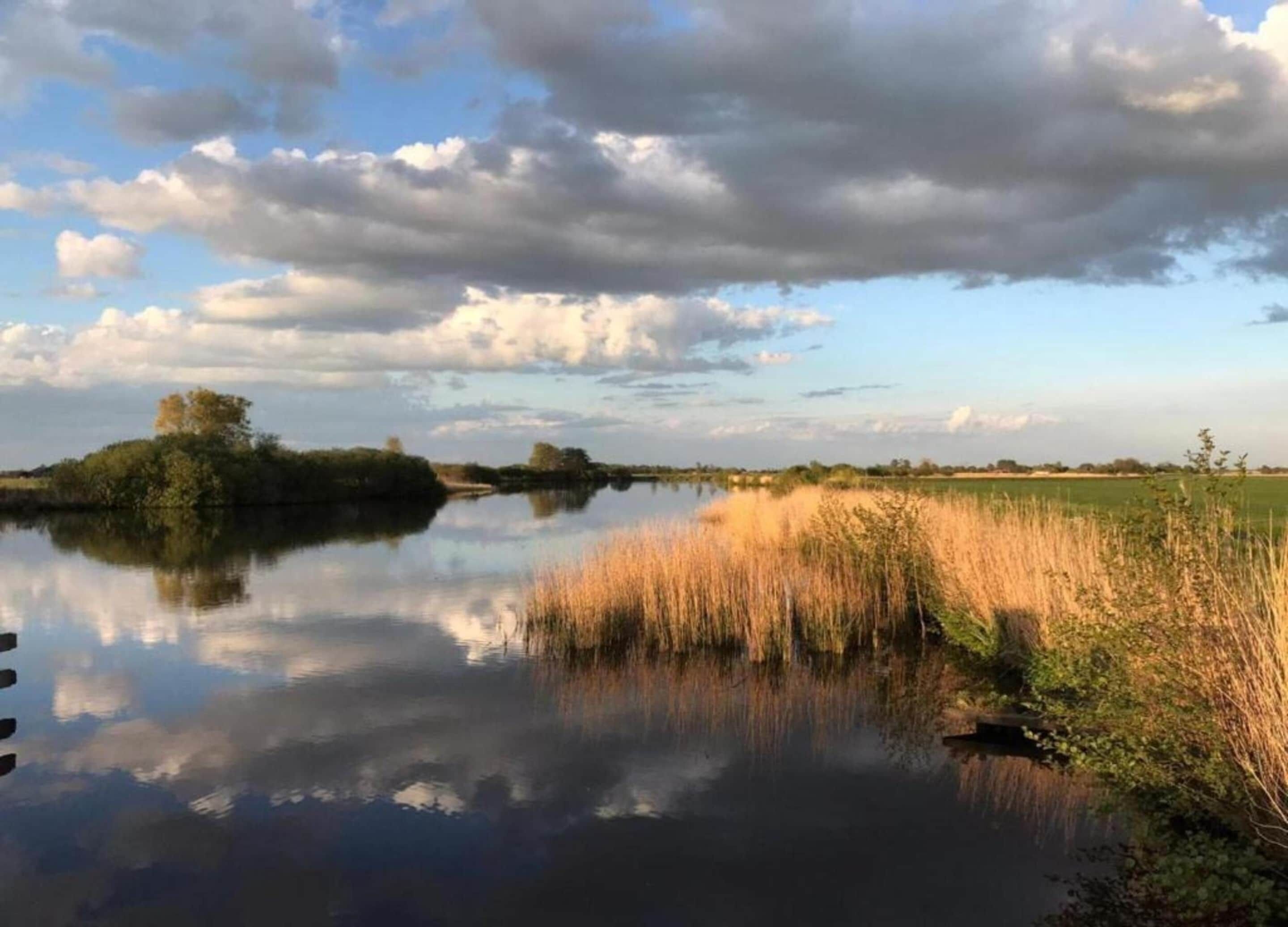 A calm river with reflections of the sky and surrounding vegetation.