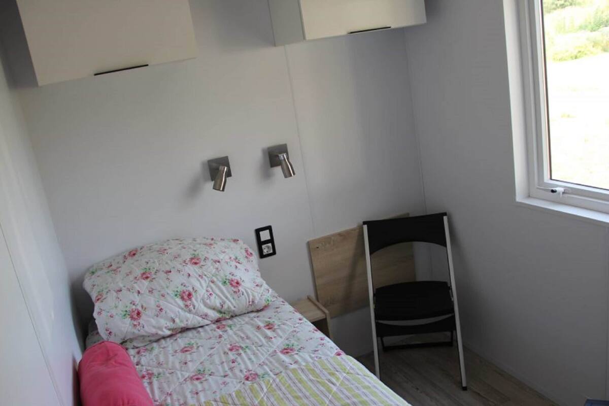 A small, neatly arranged bedroom with a bed, a chair, and a window.
