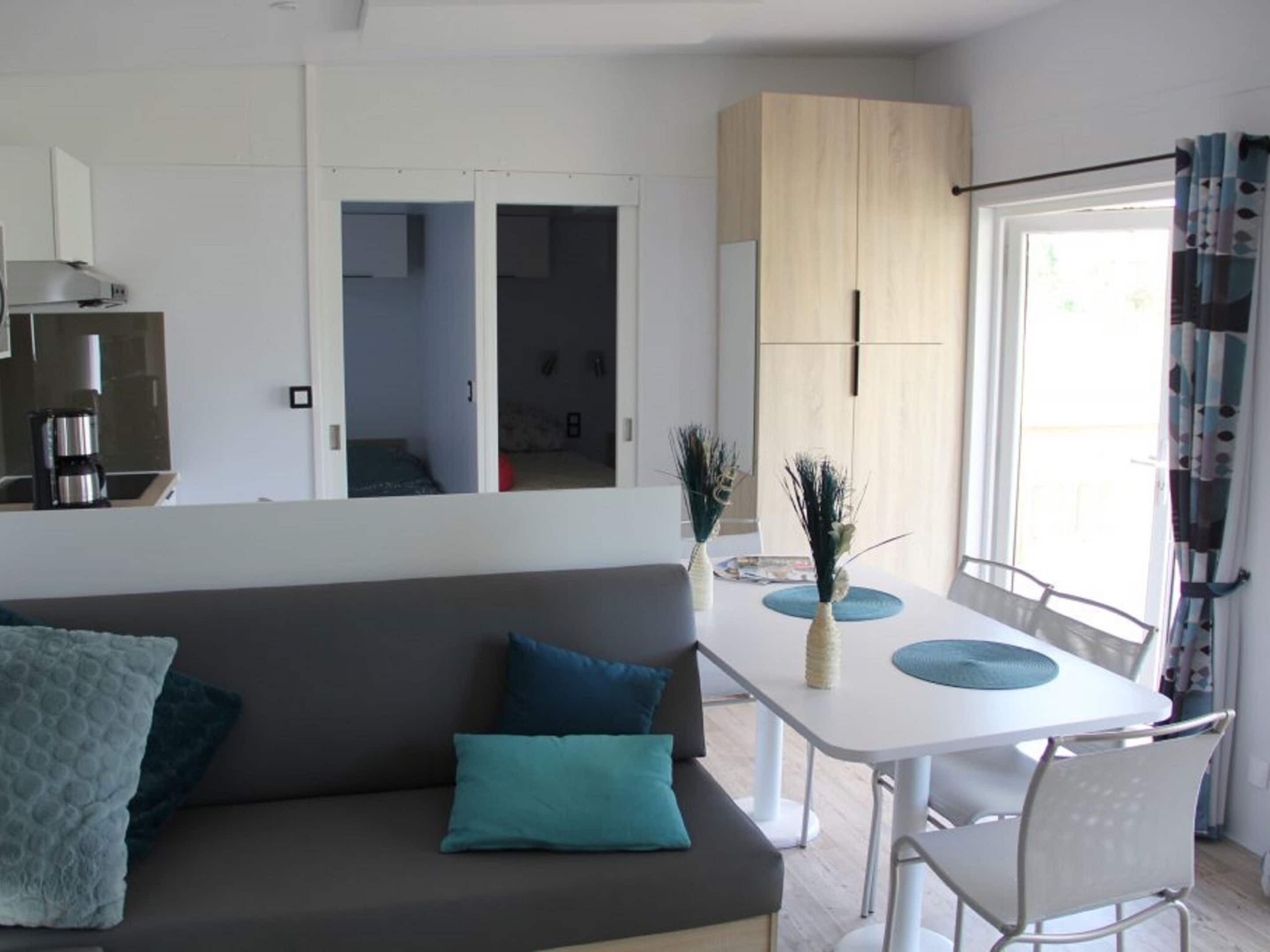 A modern living room with a sofa, a dining table with chairs, and a kitchen area visible through an open door.