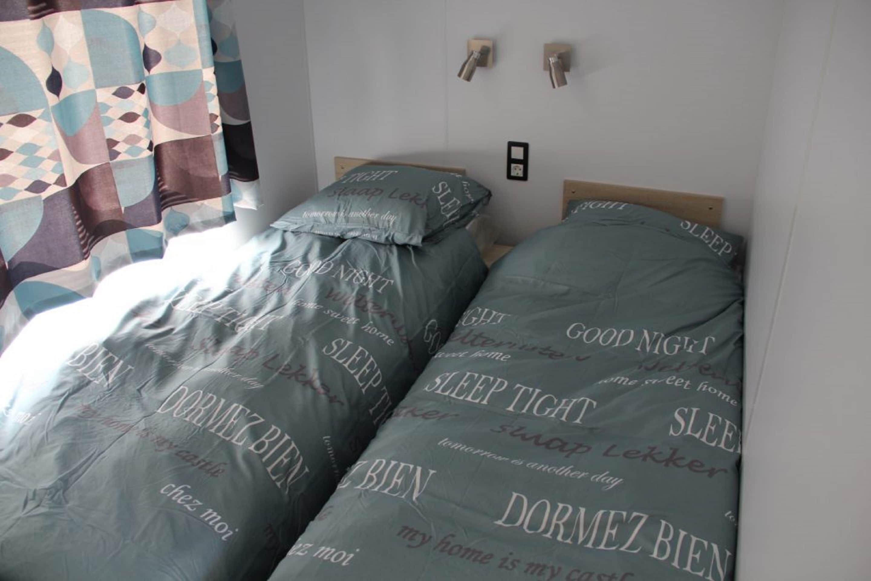 A bedroom with two beds, each covered with a blanket featuring the text "SLEEP TIGHT" and "DORMEZ BIEN".