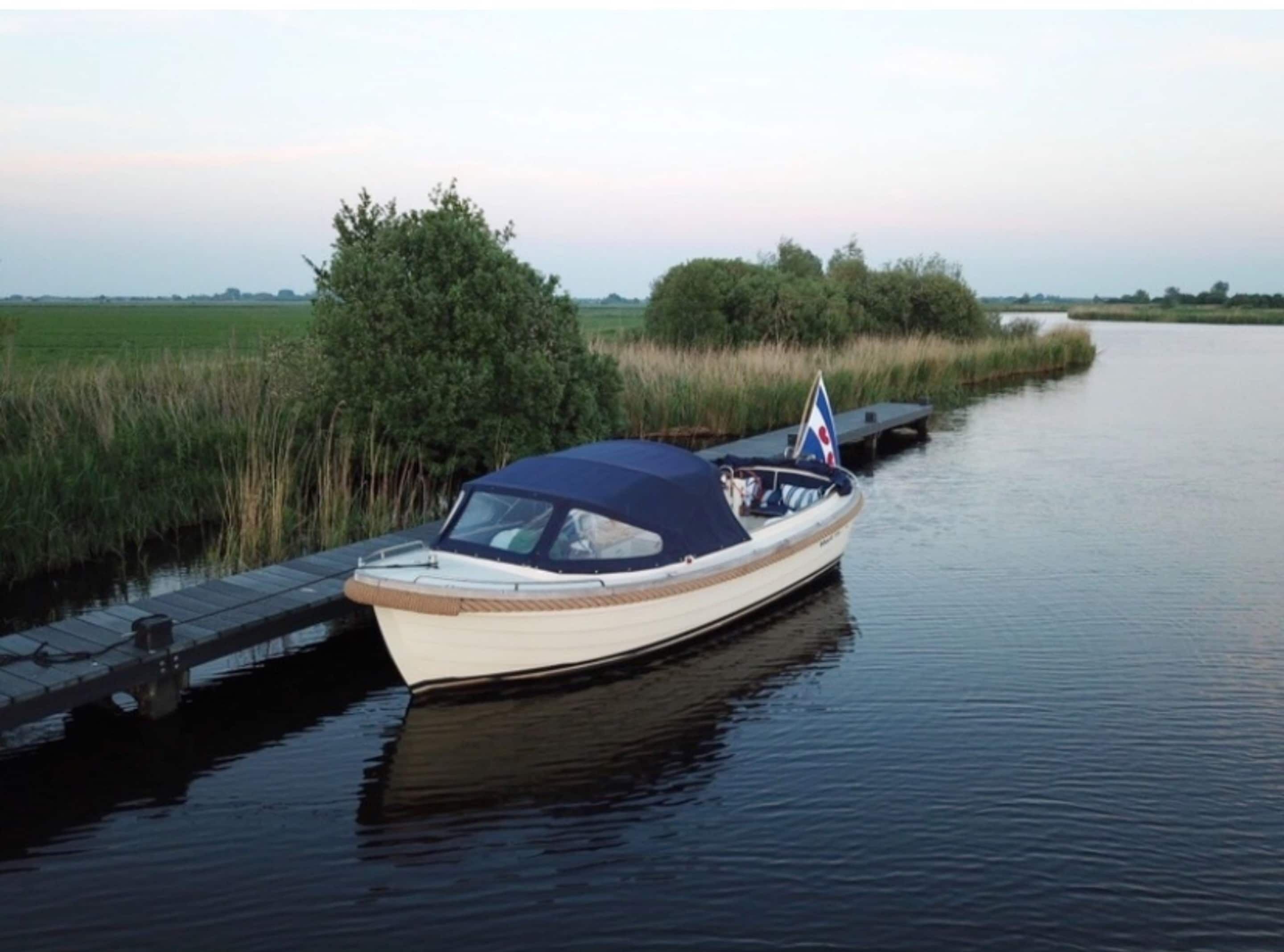 A narrow waterway with a boat docked on the left, surrounded by greenery and a clear sky.