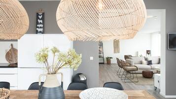A modern kitchen with a wooden dining table, a vase with flowers, and a large woven light fixture.