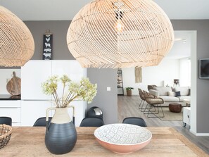 A modern kitchen with a wooden dining table, a vase with flowers, and a large woven light fixture. - Modern Apartment With a View of the Scheveningen Harbor (The Hague)