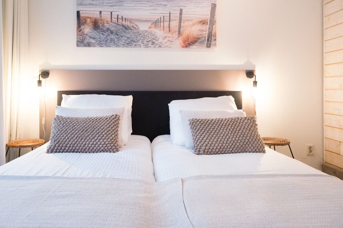 A double bed with a dark headboard, two bedside tables, and a wall-mounted picture of a beach scene.