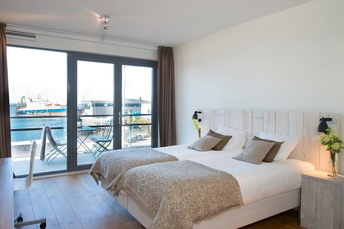 A modern bedroom with a large bed, a view of the sea, and a balcony with outdoor furniture.