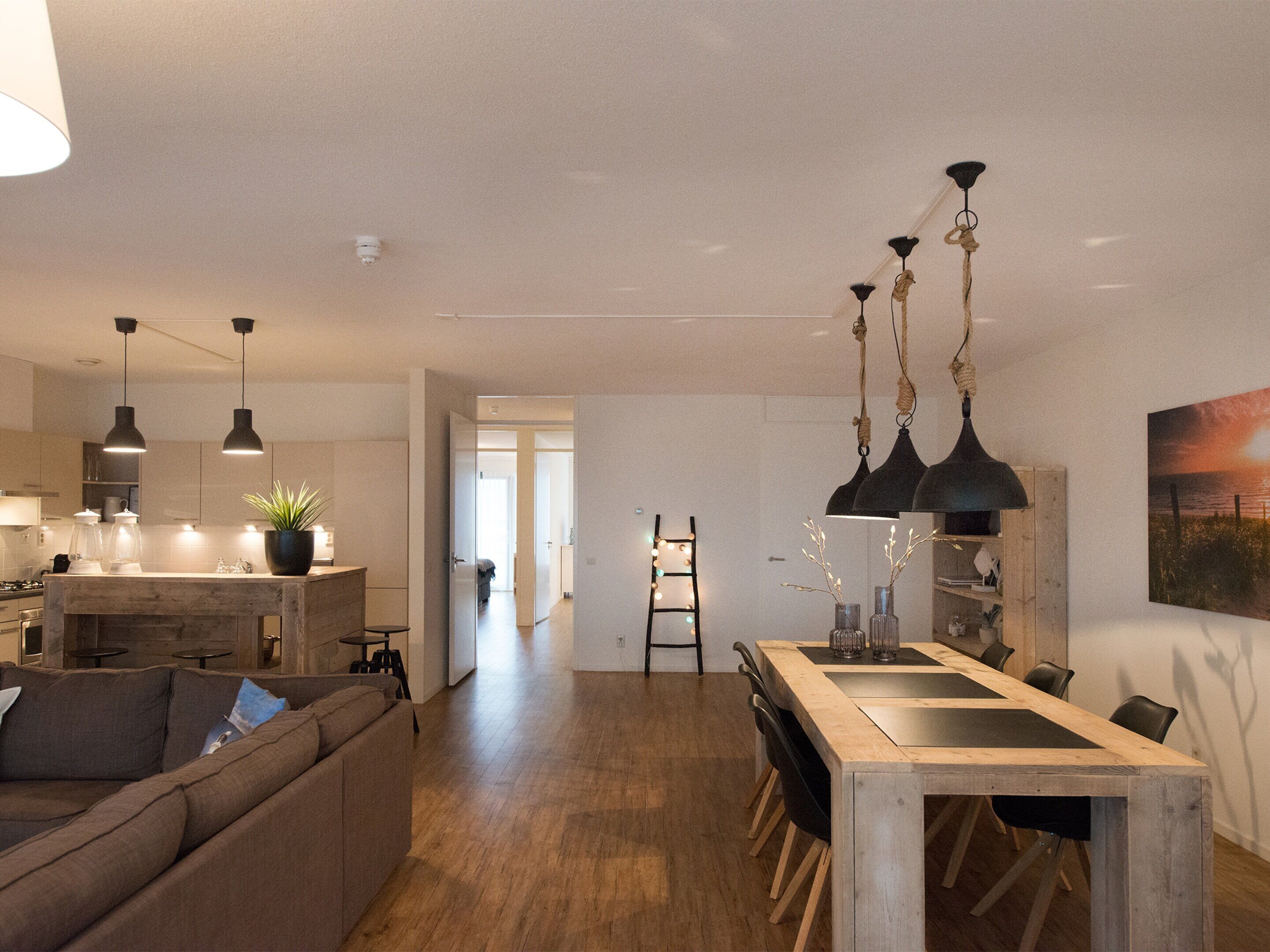 A modern kitchen with wooden countertops, a dining area with a large table and chairs, and a living room with a sofa.