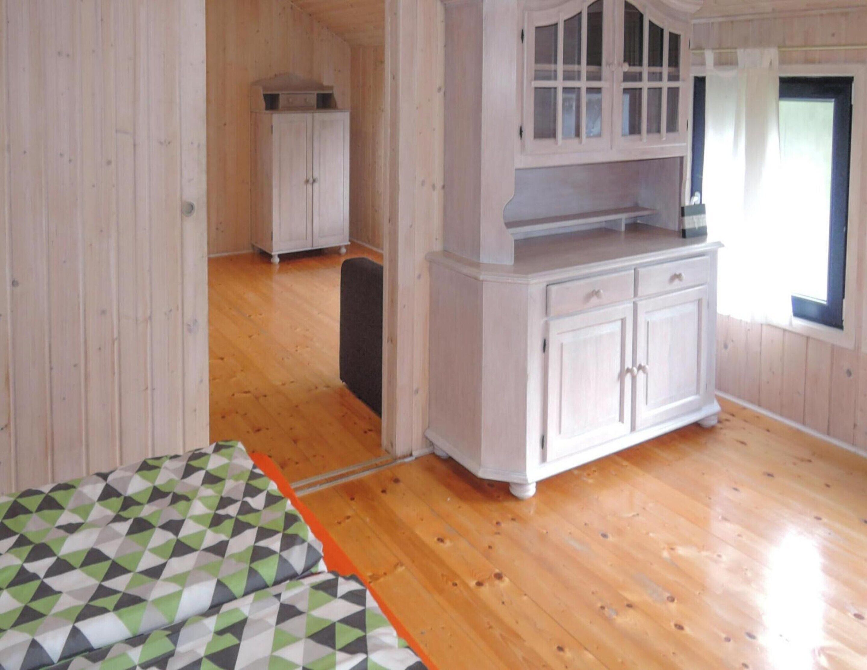 Une pièce dotée d’un plancher en bois, d’un lit recouvert d’une couvre-lit à motifs géométriques, d’une armoire blanche et d’une fenêtre avec des rideaux.