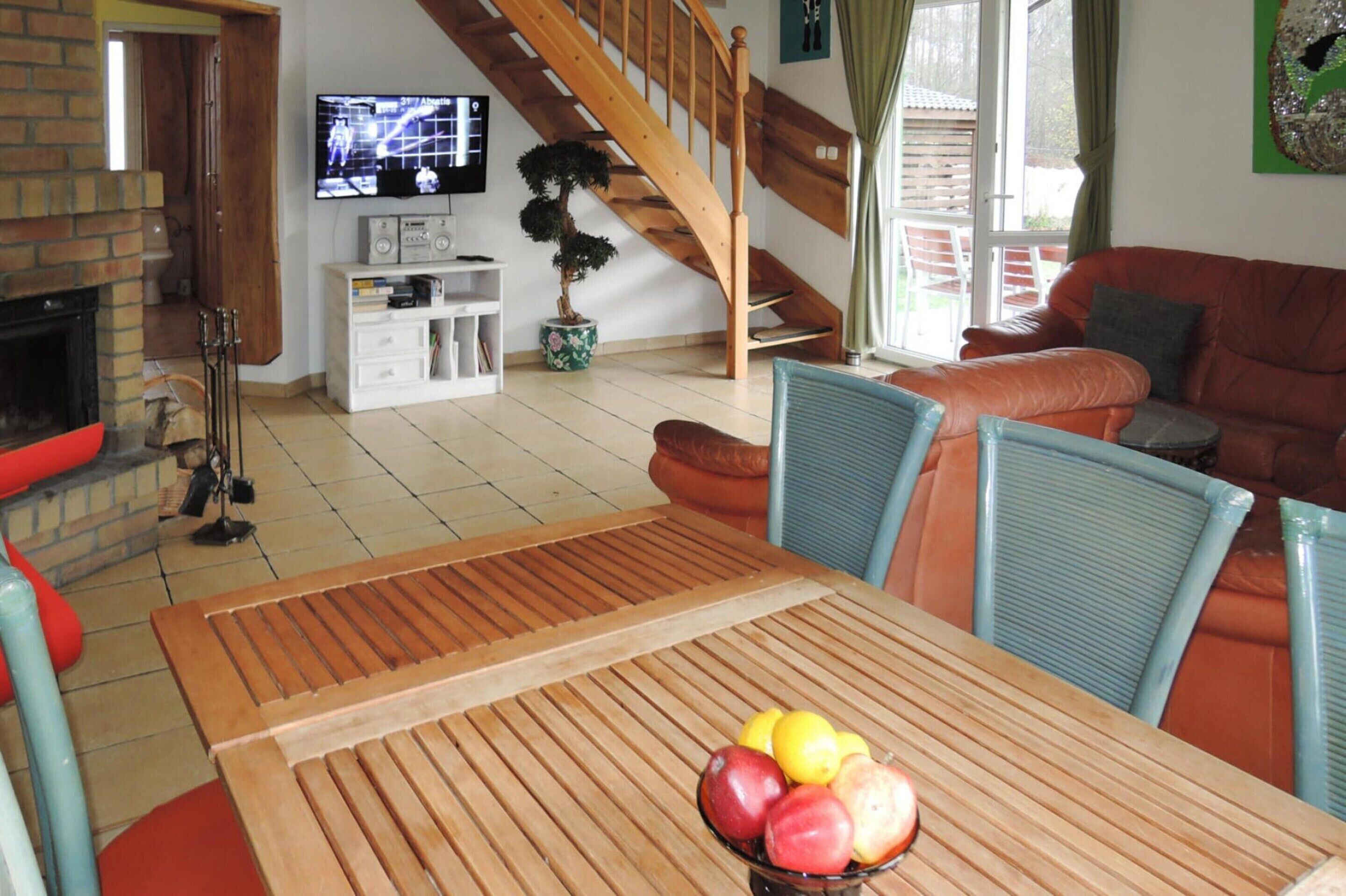 Una sala de estar con una mesa de madera, un sofá, un televisor, una escalera y una planta en maceta.